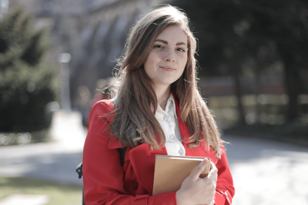 College Student standing in campus with a book