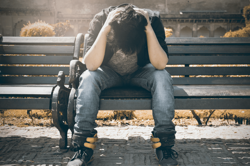 Man with head in hands sitting on a park bench