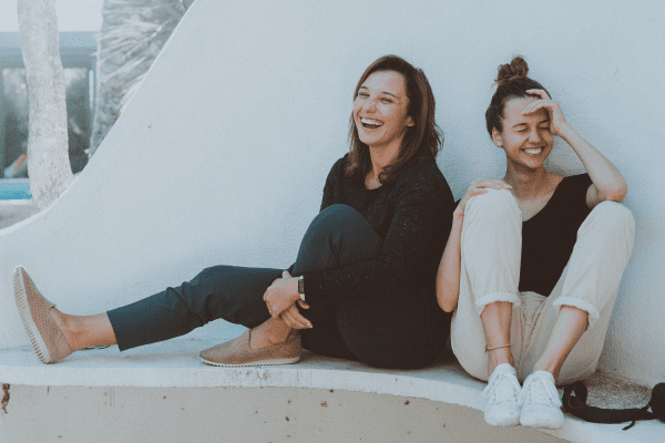 Mother and daughter sitting by each other laughing