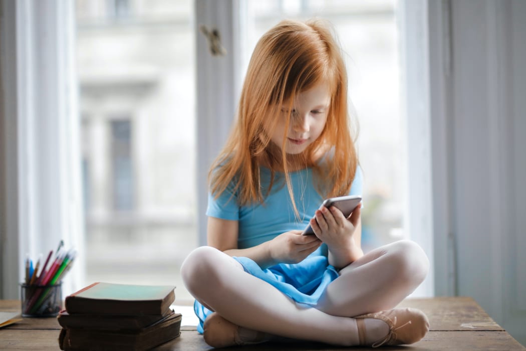 red haired girl sitting on a table looking at a cell phone