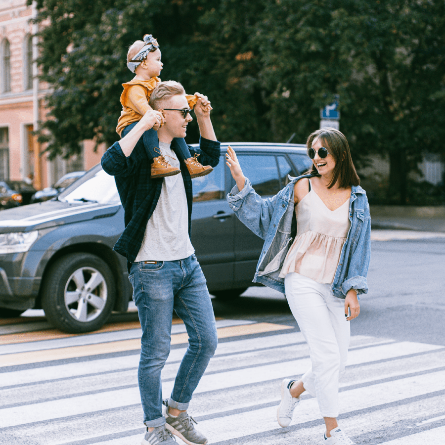 Daughter sitting on her fathers shoulders as he walks across a street with his wife