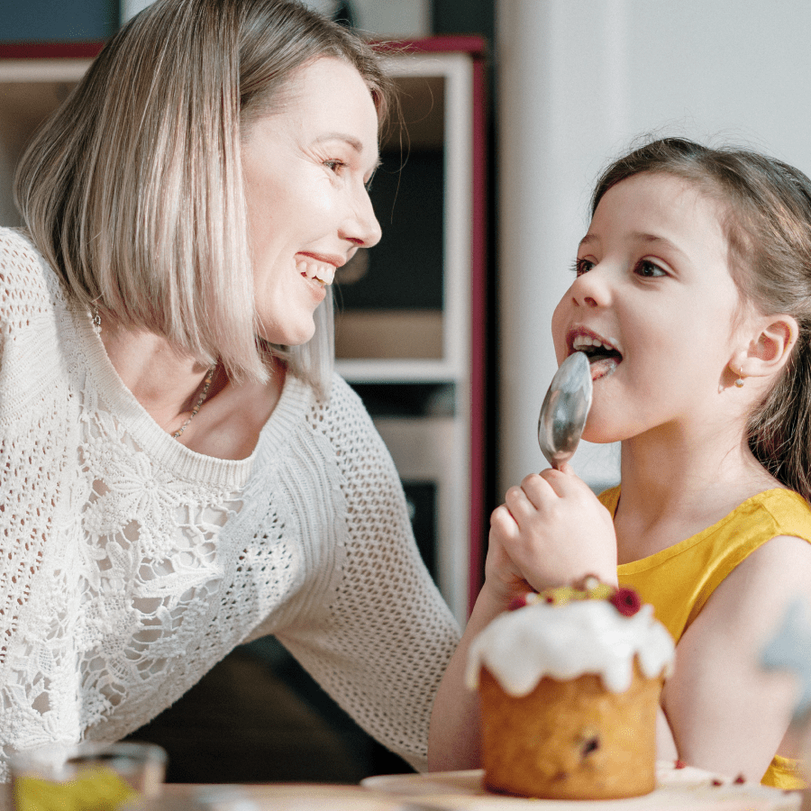 Mother watching her daughter lick a spoon with cupcake icing on it