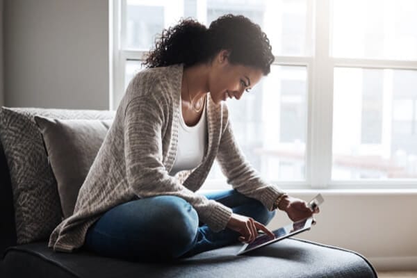 woman sitting on a couch and using an iPad to do her banking