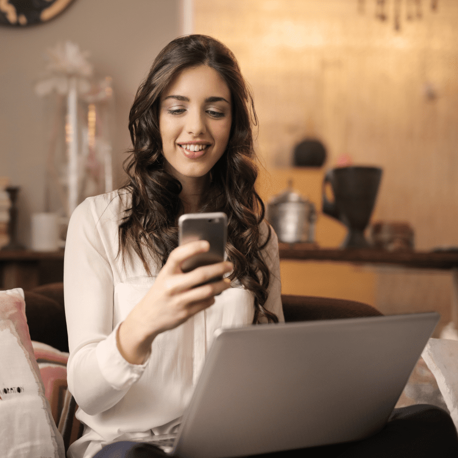 woman looking at cell phone while at her computer