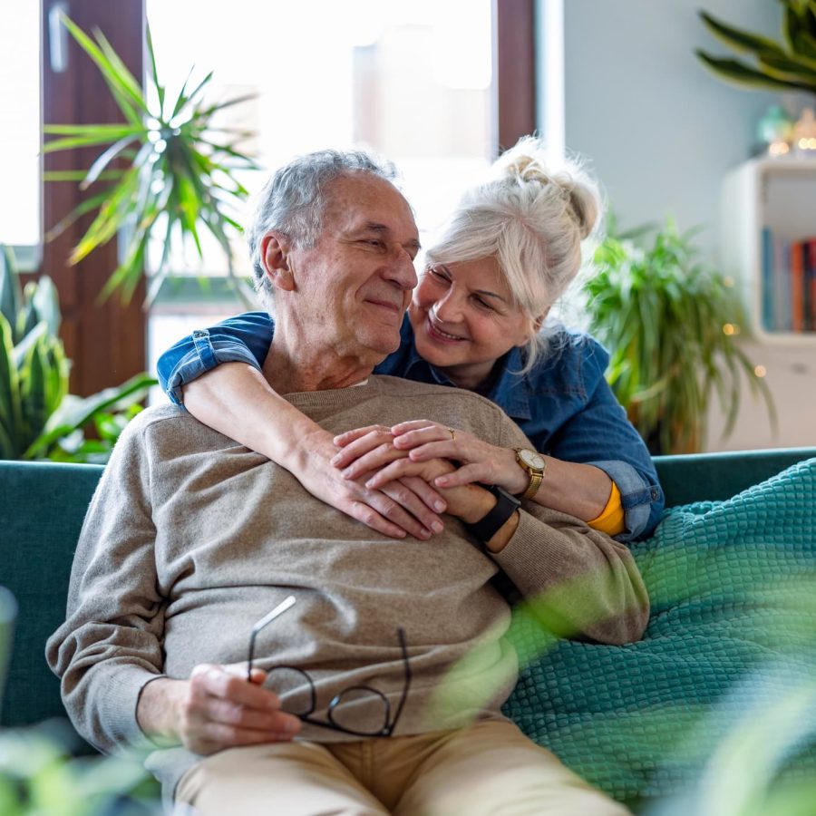 older couple cuddling in a room with plants