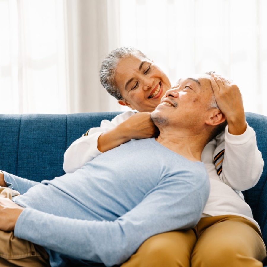 Husband lay on his wife's lap sitting on the couch in living room with happy, comfortable and relationship lifestyle, Senior Asian couple at home