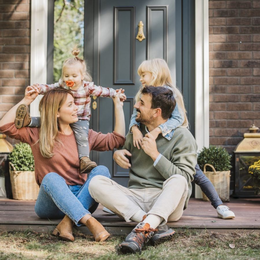 Young family with two kids having fun in front of there house. Porch is decorated with flowers.