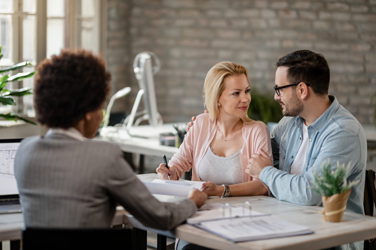 a couple is looking each other in the eyes as they're about to sign their paperwork on a mortgage.