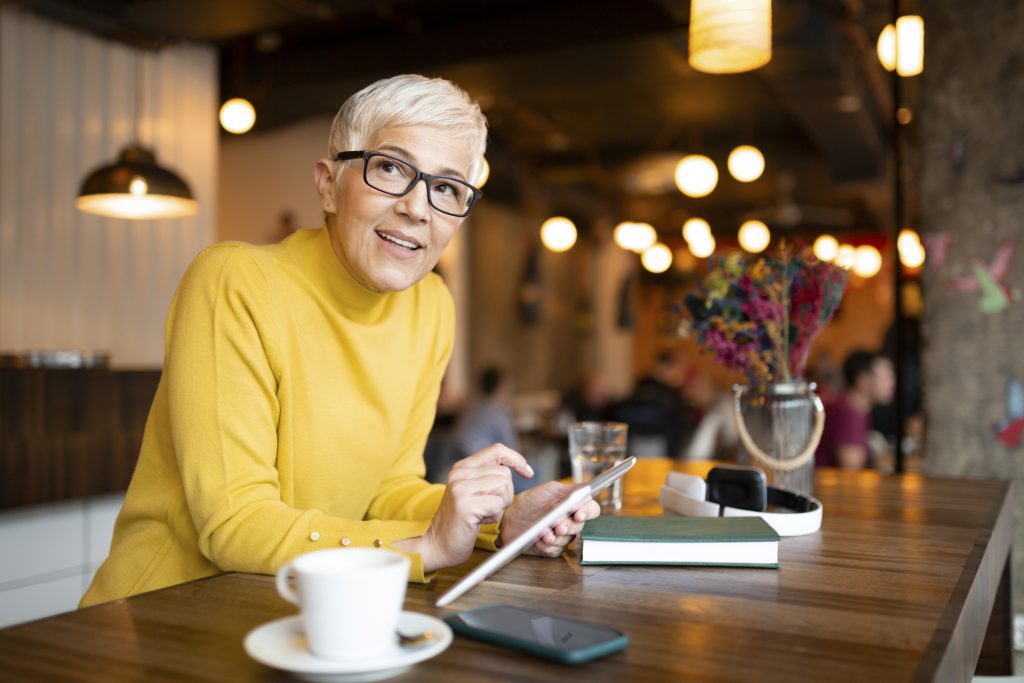 an older woman is looking at her tablet at a standing table.
