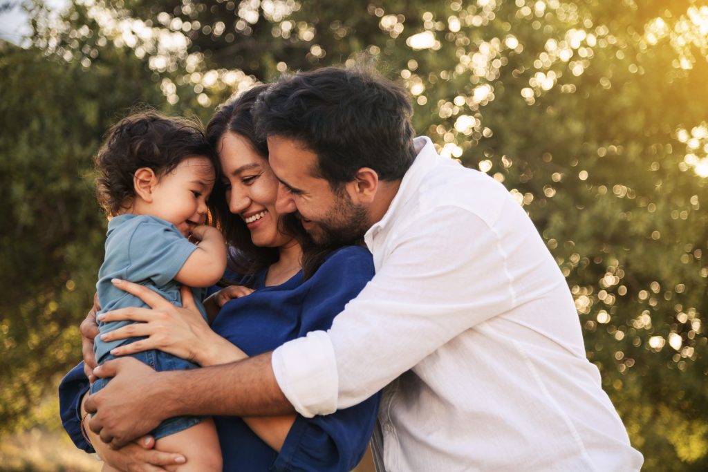 A young family is hugging their young child in the backyard of their new house.